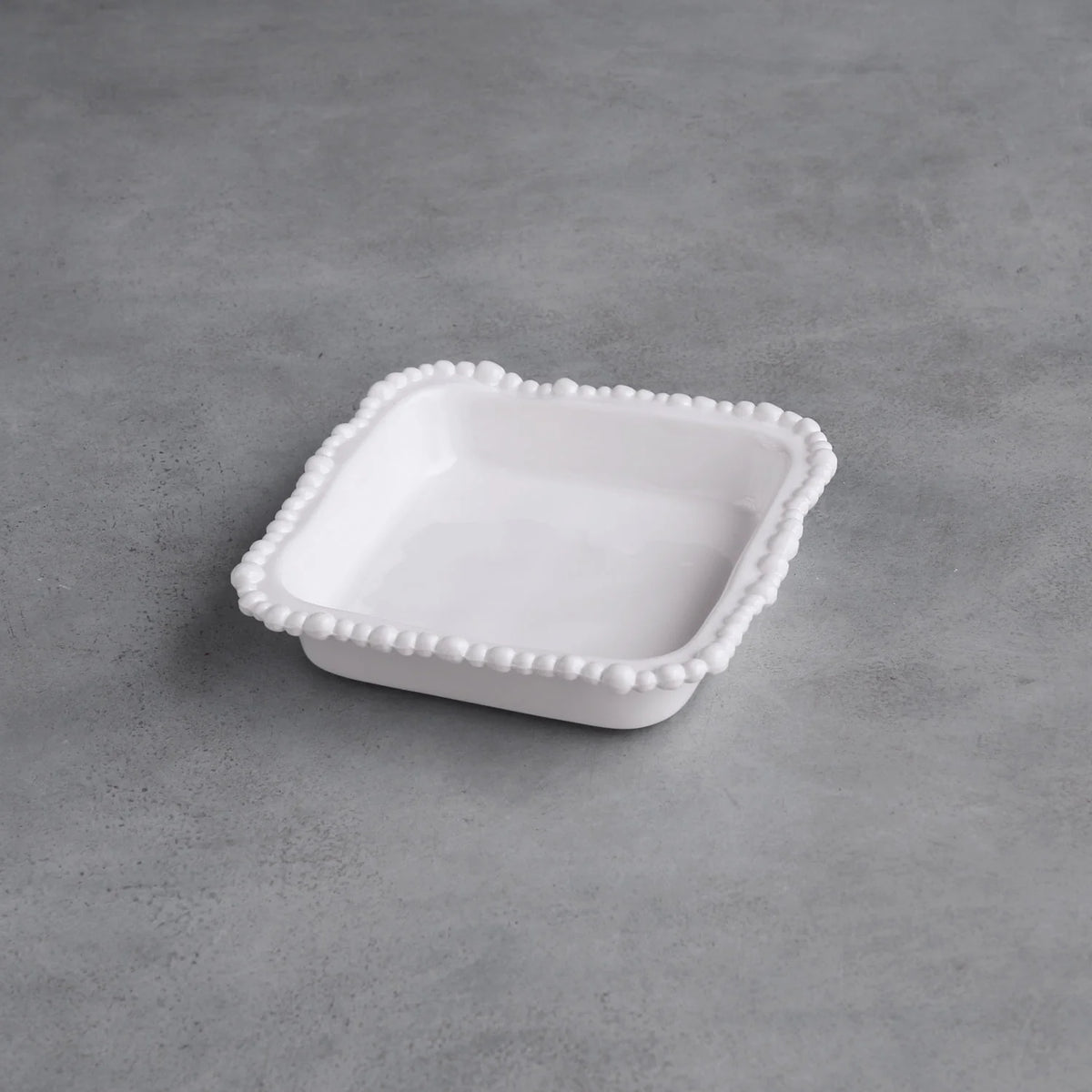 White ceramic dish with decorative edge on a gray concrete surface