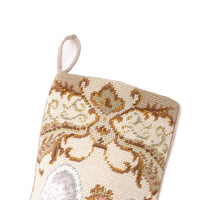 Close-up of handcrafted wool needlepoint embroidery showing ornate golden scrollwork and decorative details on an ivory Christmas stocking