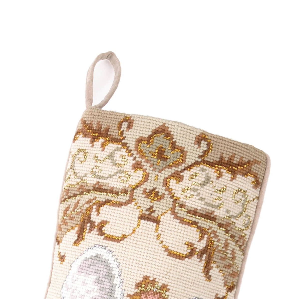Close-up of handcrafted wool needlepoint embroidery showing ornate golden scrollwork and decorative details on an ivory Christmas stocking