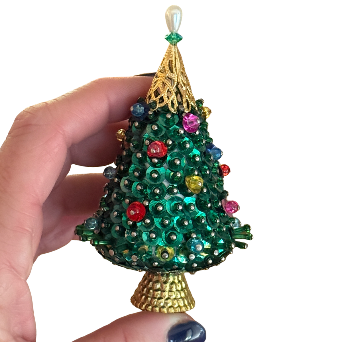 Hand-held close-up of a vintage green sequin Christmas tree ornament showing colorful pinned beads, an openwork gold-tone top, and a textured base.