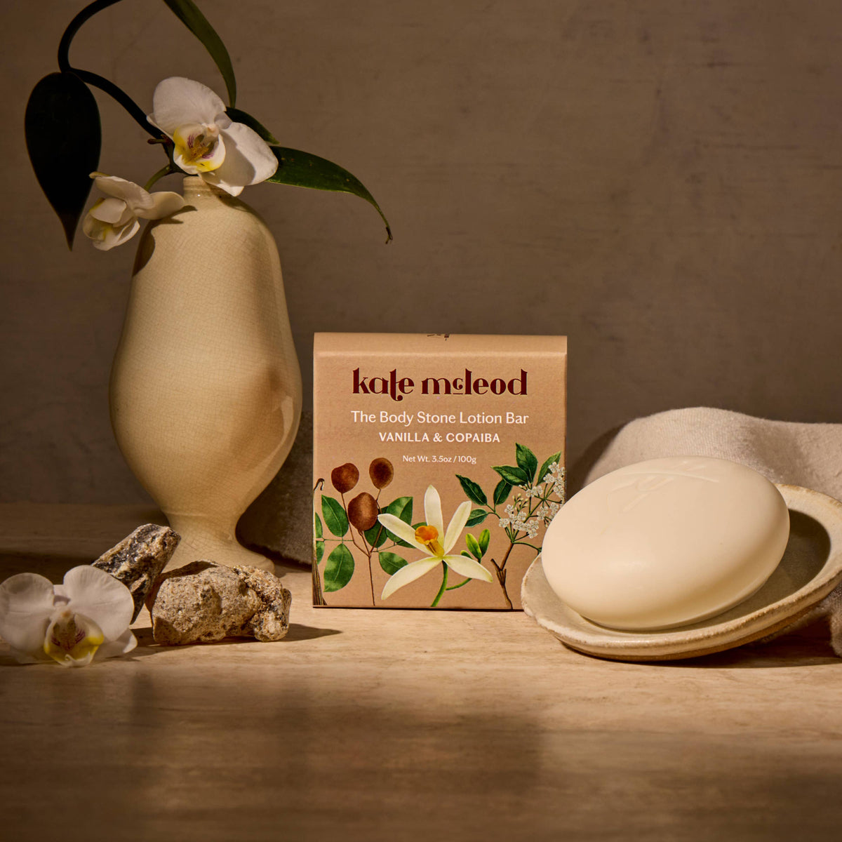 Kate McLeod Vanilla & Copaiba Body Stone solid lotion bar with botanical packaging and round white moisturizing bar.