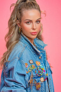 Woman wearing a denim jacket with colorful patches against a pink background