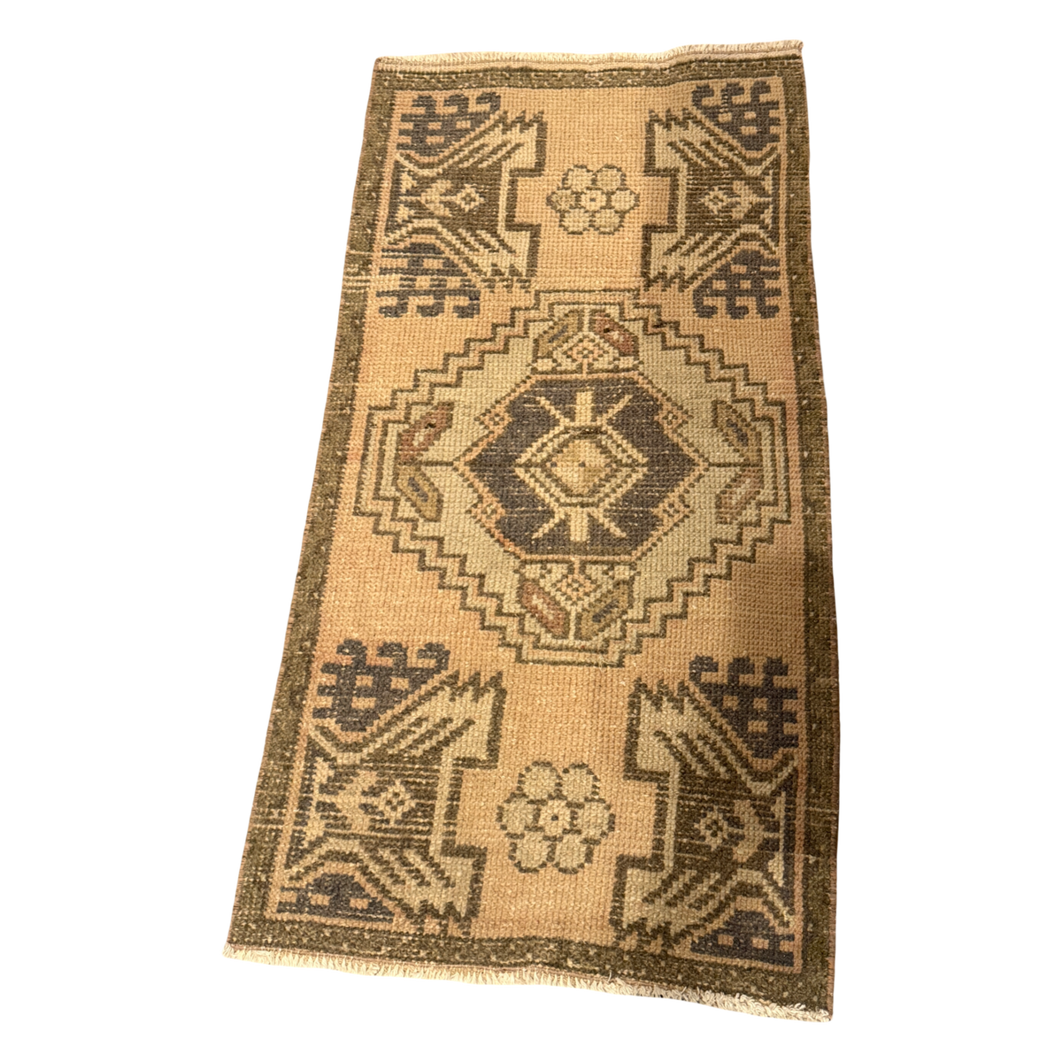Warm apricot mini rug with a charcoal-centered cream and olive medallion, mirrored geometric corner motifs, small rosettes, and cream fringe.