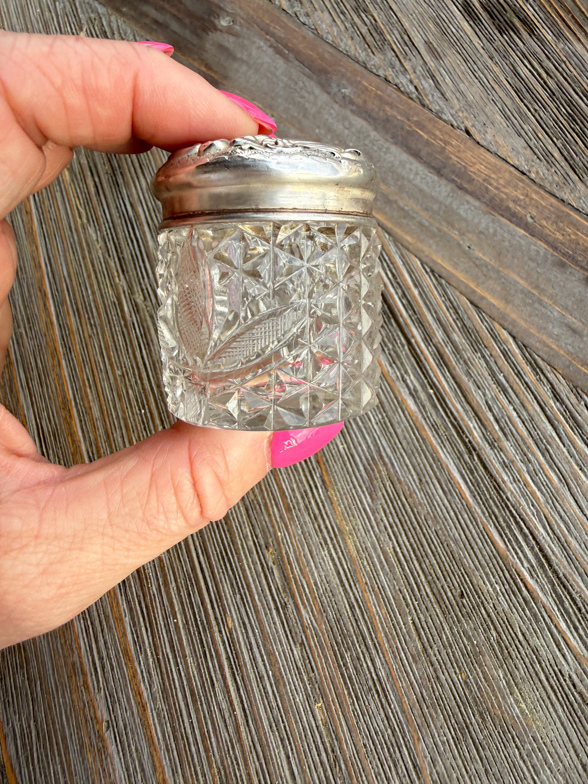 Hand holding a decorative glass container with a silver base on a wooden surface