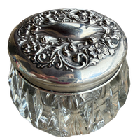 Decorative glass jar with an ornate silver lid on a white background