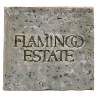 A single rectangular bar of handmade soap with a rustic, textured surface speckled with dark flecks. The brand name 'FLAMINGO ESTATE' is embossed in the center of the soap.