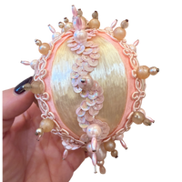 handmade vintage Christmas ornament featuring ivory satin, blush pink pearl embellishments, delicate gold trim, and dangling pink beads.