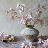 Pink flowers in a textured vase on a lace tablecloth with a floral background