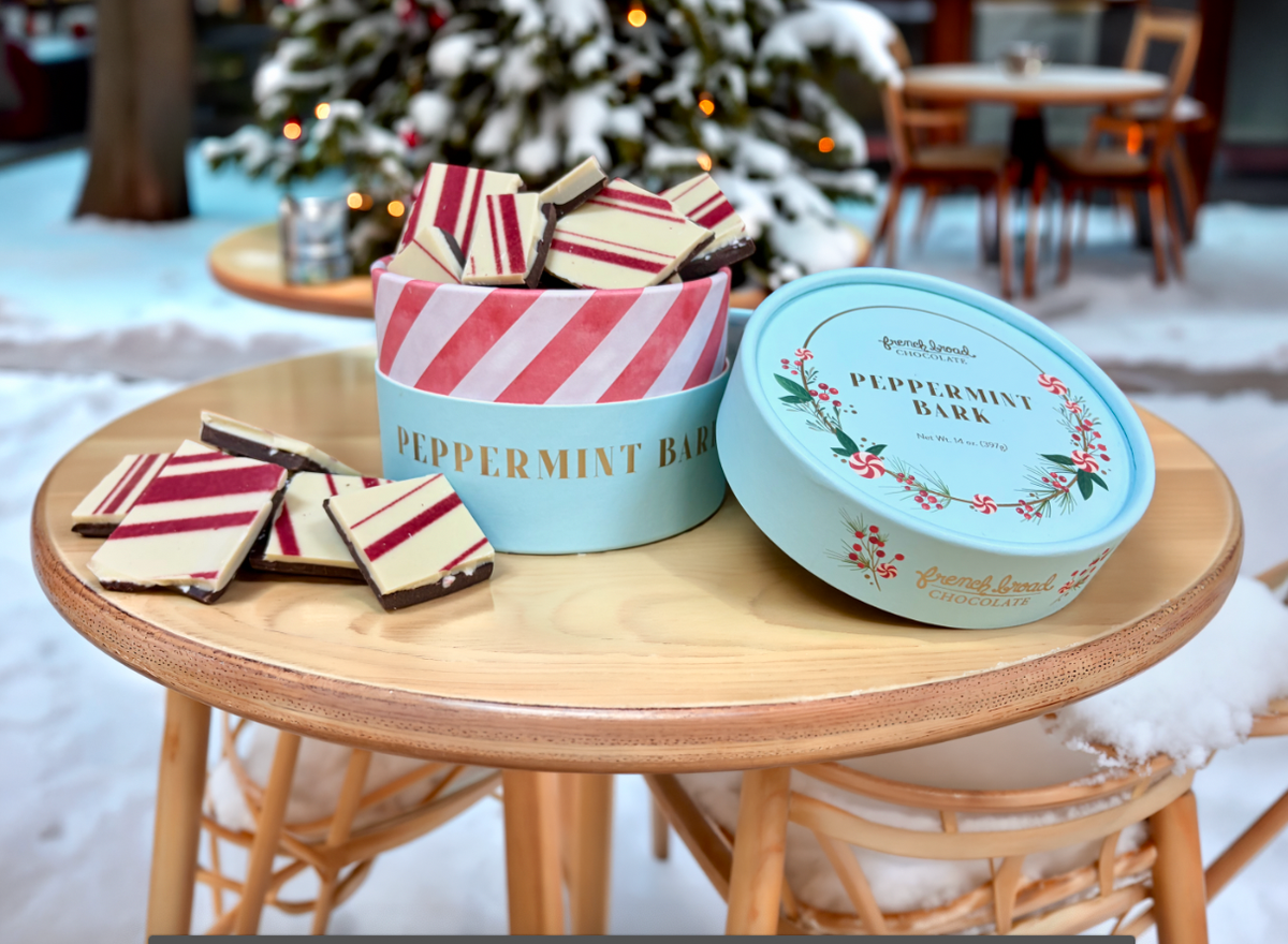 French Broad Chocolate peppermint bark in decorative holiday tin displayed with Christmas decorations and peppermint chocolate pieces