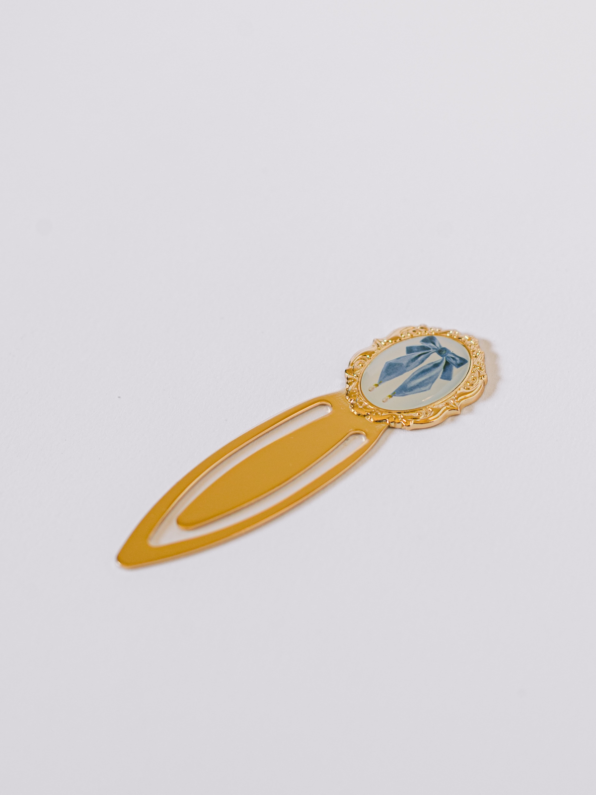 Gold-tone metal clip bookmark featuring antique blue bow illustration and decorative resin accent