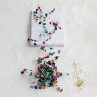 Multicolored holographic confetti garland with small reflective circular accents along a slender strand, shown vertically against a white background.