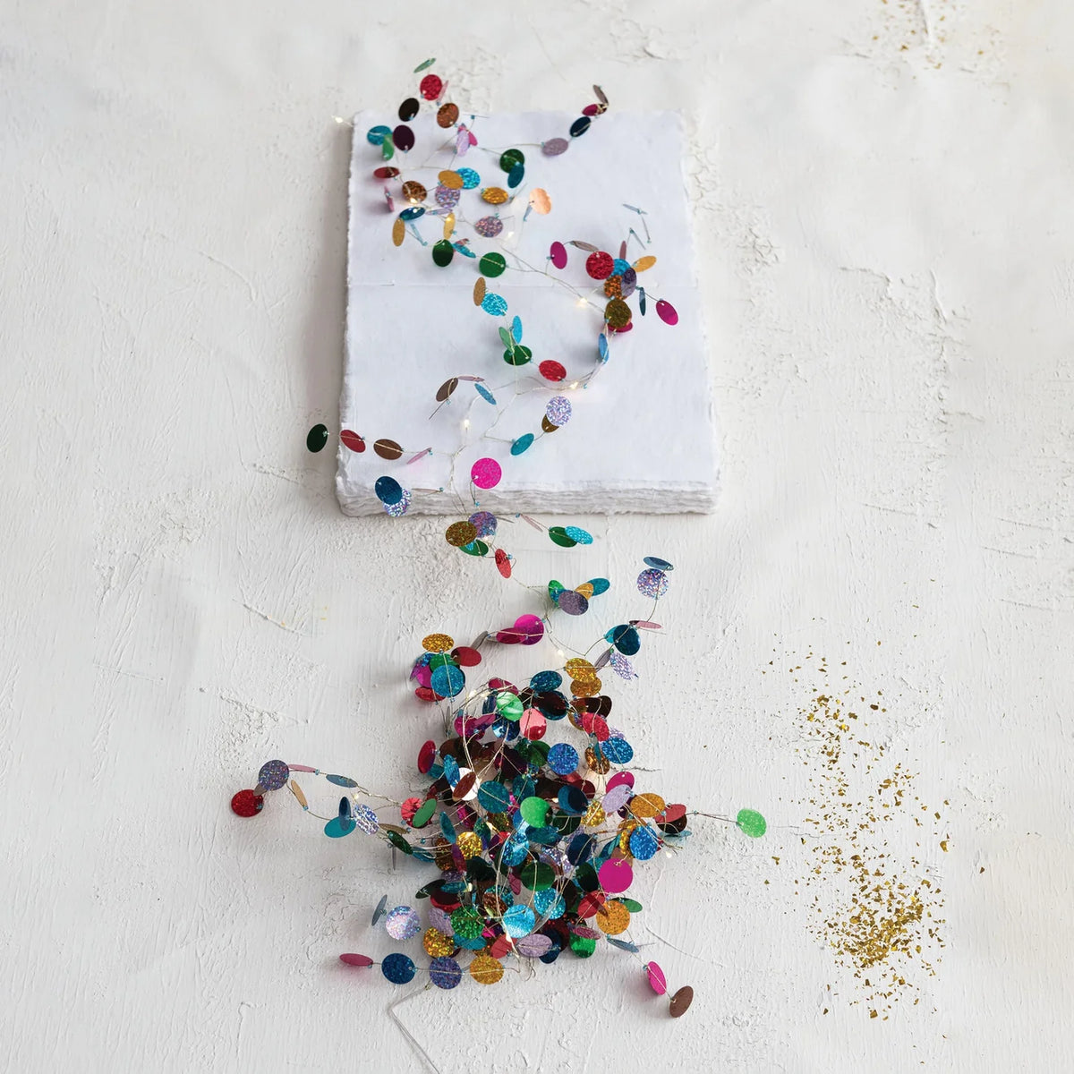 Multicolored holographic confetti garland with small reflective circular accents along a slender strand, shown vertically against a white background.