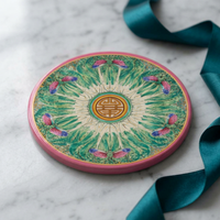 Round sandstone coaster with a pink border, green bok choy-inspired pattern, and dragonfly details on a marble surface.