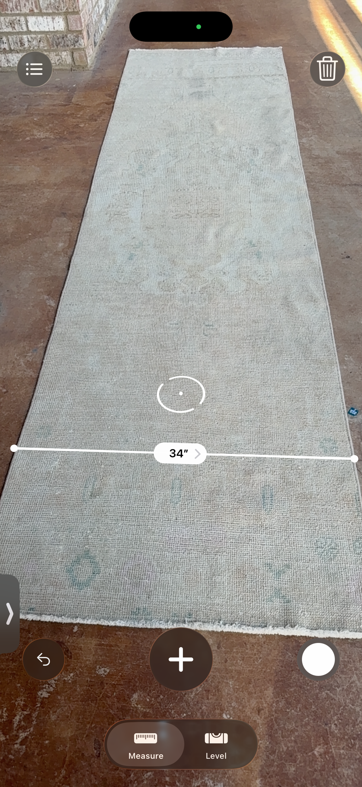 A long rectangular area rug laid flat on a brown floor, shown from above with a white measurement overlay indicating 34 inches in width.