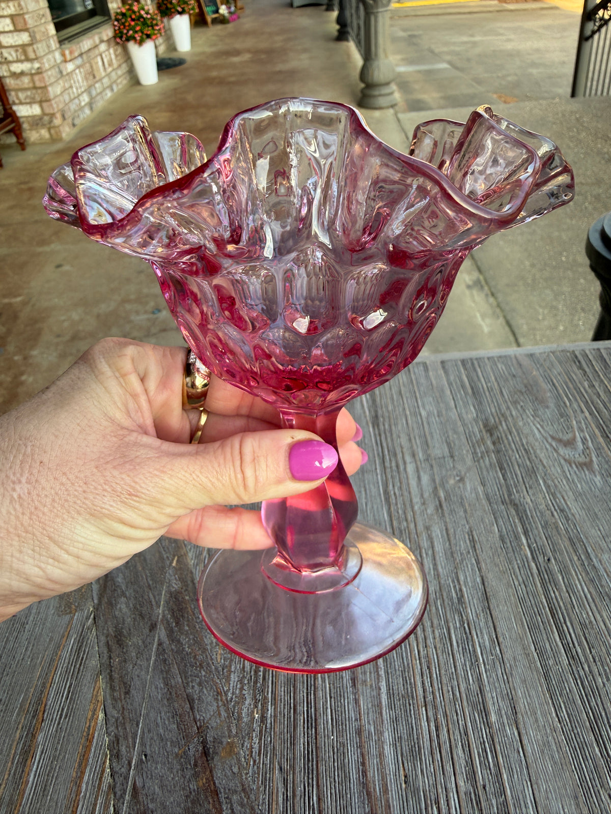 Hand holding a pink crystal glass against a wooden surface