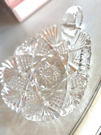 Clear glass candy dish with intricate patterns on a light wooden surface