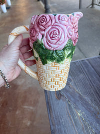 Cat-shaped mug with floral design held by a hand against a wooden surface.
