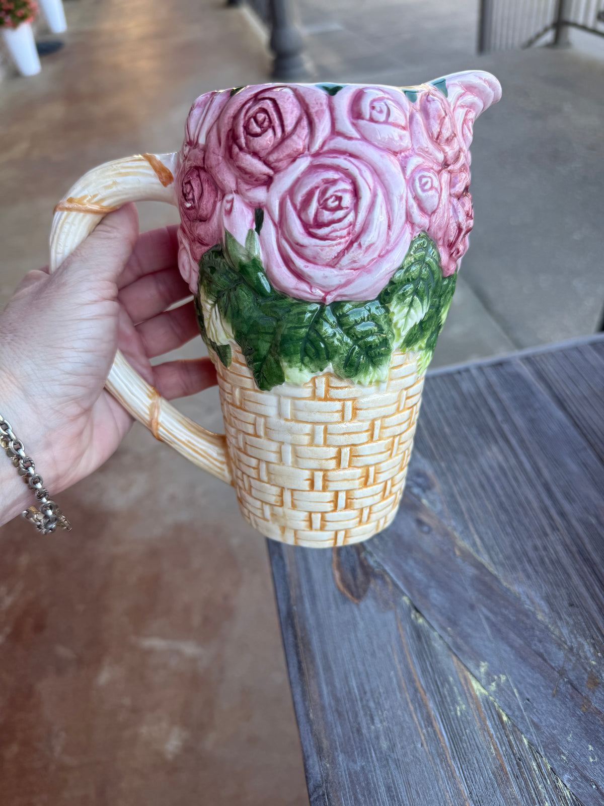 Cat-shaped mug with floral design held by a hand against a wooden surface.